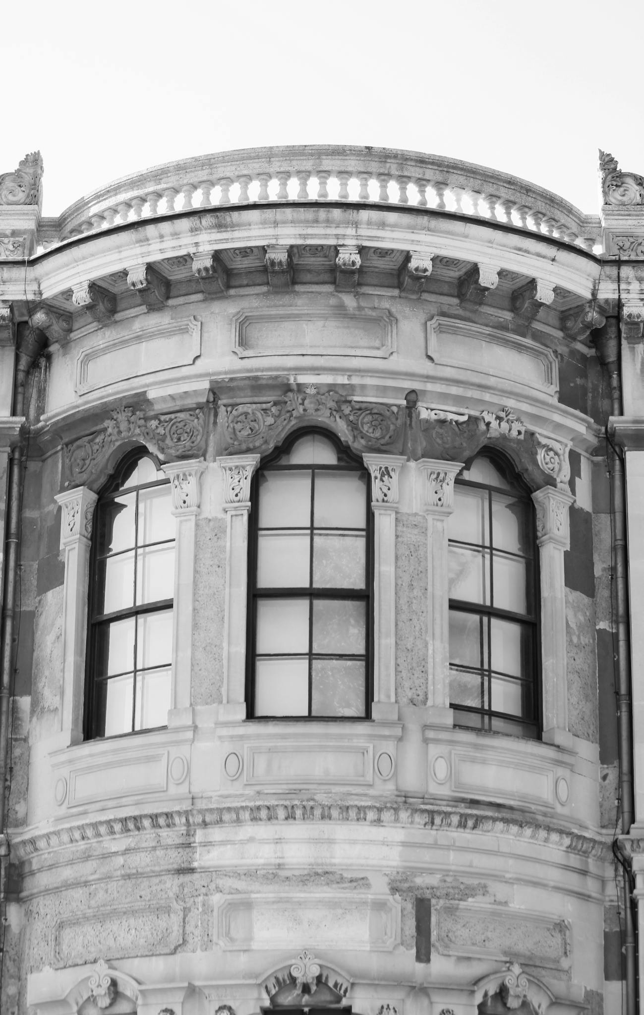 Black and white photo of a vintage facade with ornate windows, highlighting architectural details.