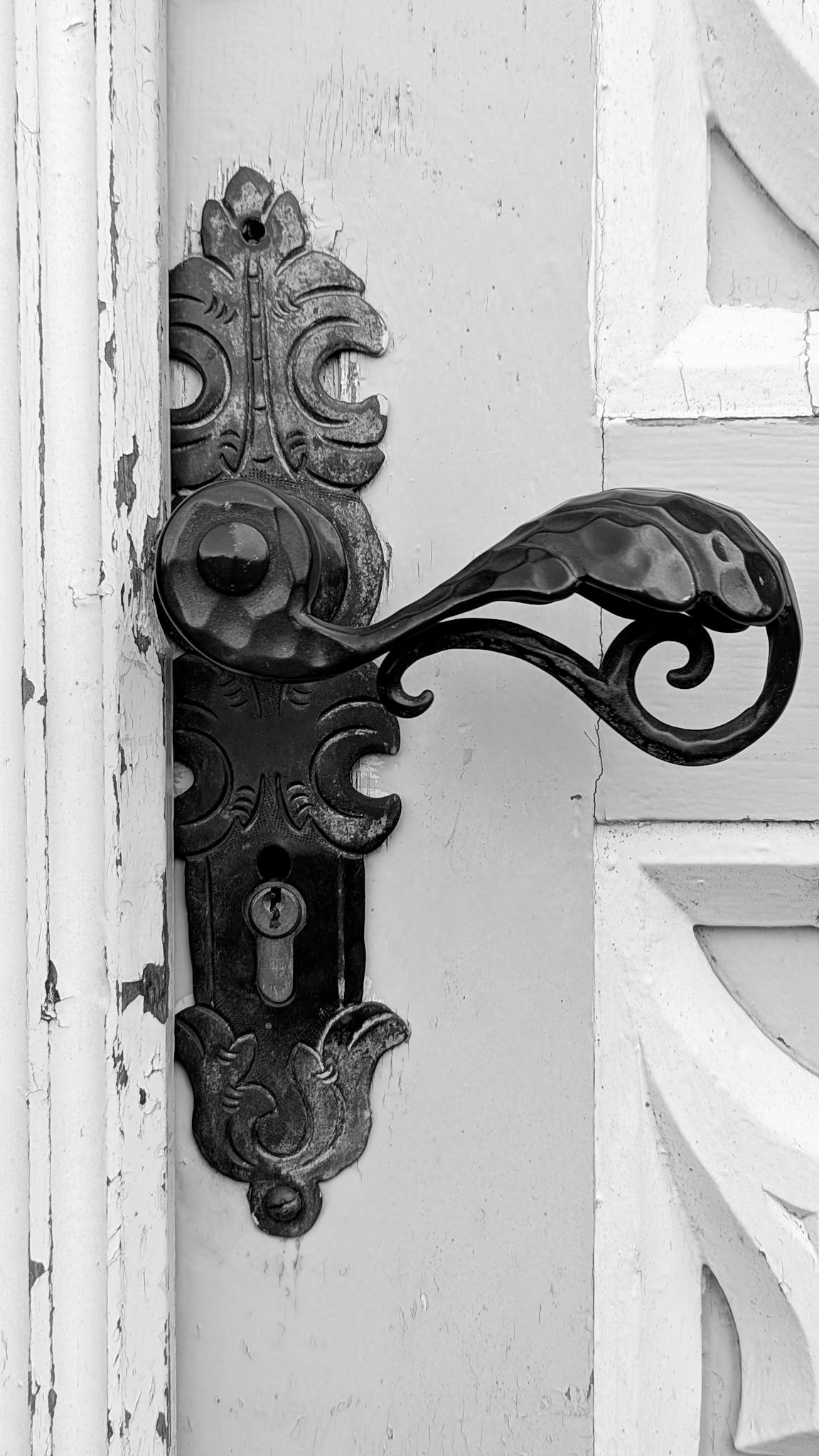 Close-up of a vintage ornate door handle in black and white, showcasing intricate metalwork.