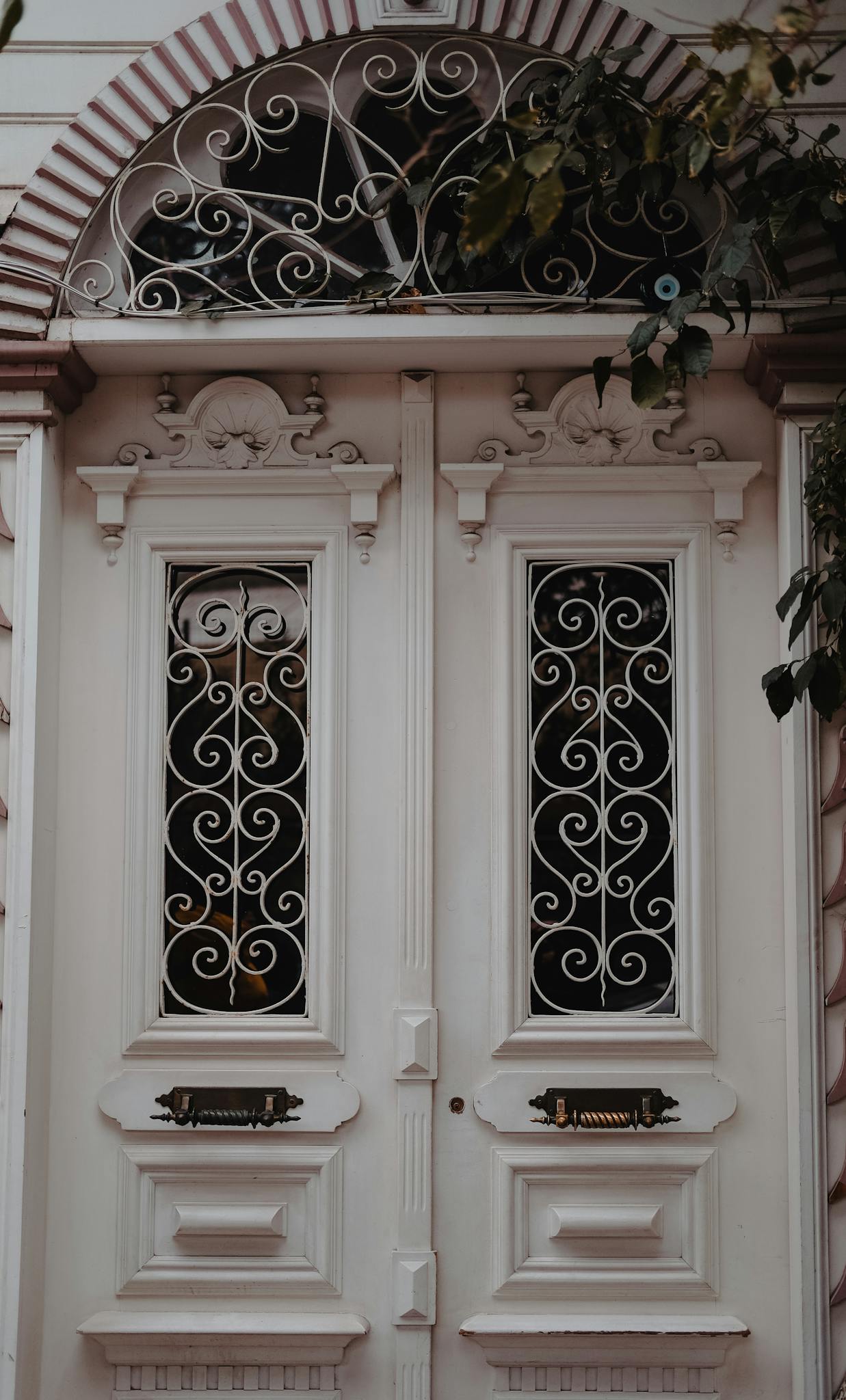 Intricate vintage white double doors with ornamental ironwork and arch design.